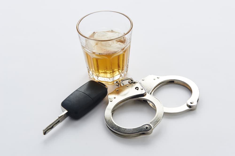 Handcuffs, whiskey, and car keys on a white background, symbolizing the dangers of drunk driving and the legal consequences that follow.