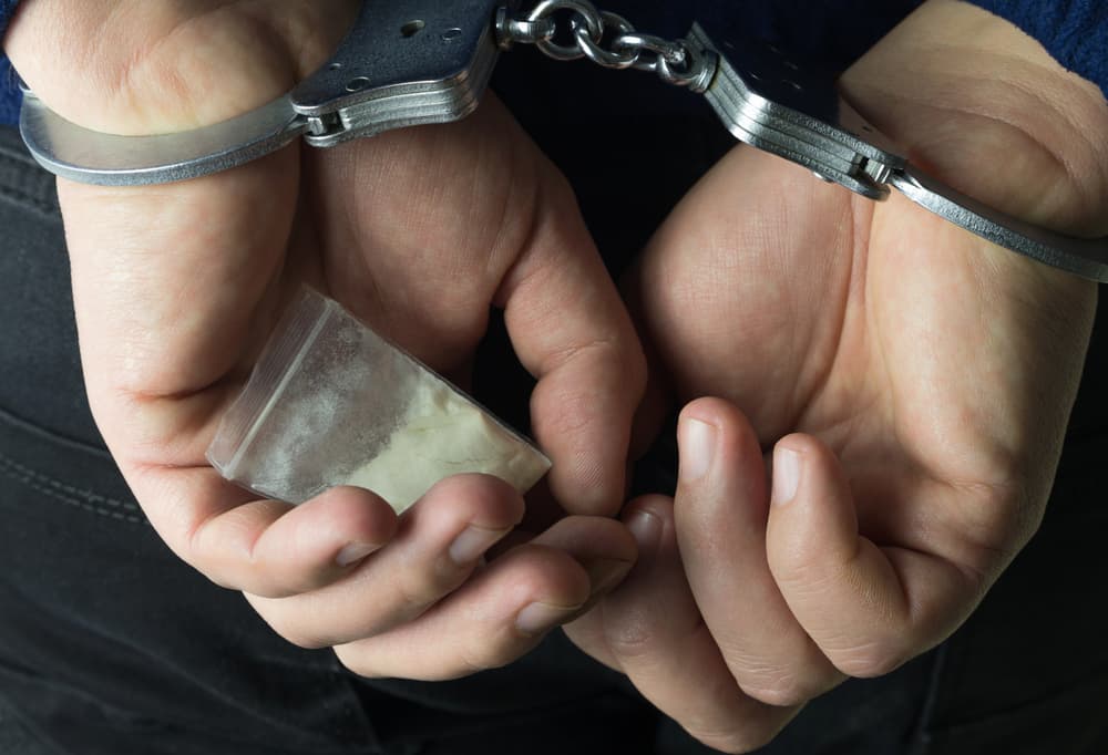 Arrested drug dealer in handcuffs with drug package.